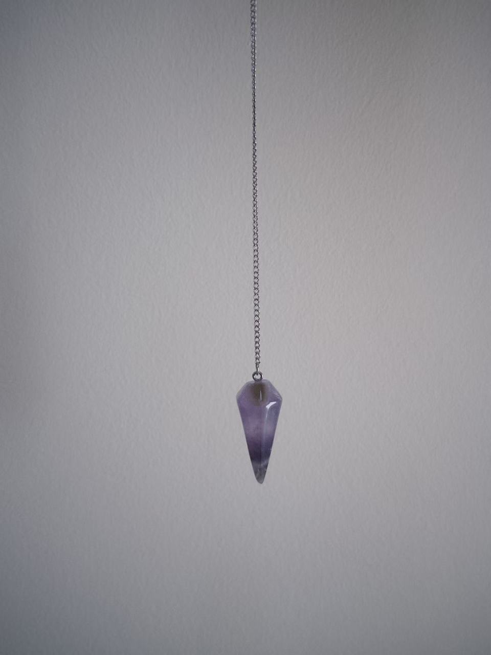 An amethyst pendulum hanging on a fine silver chain