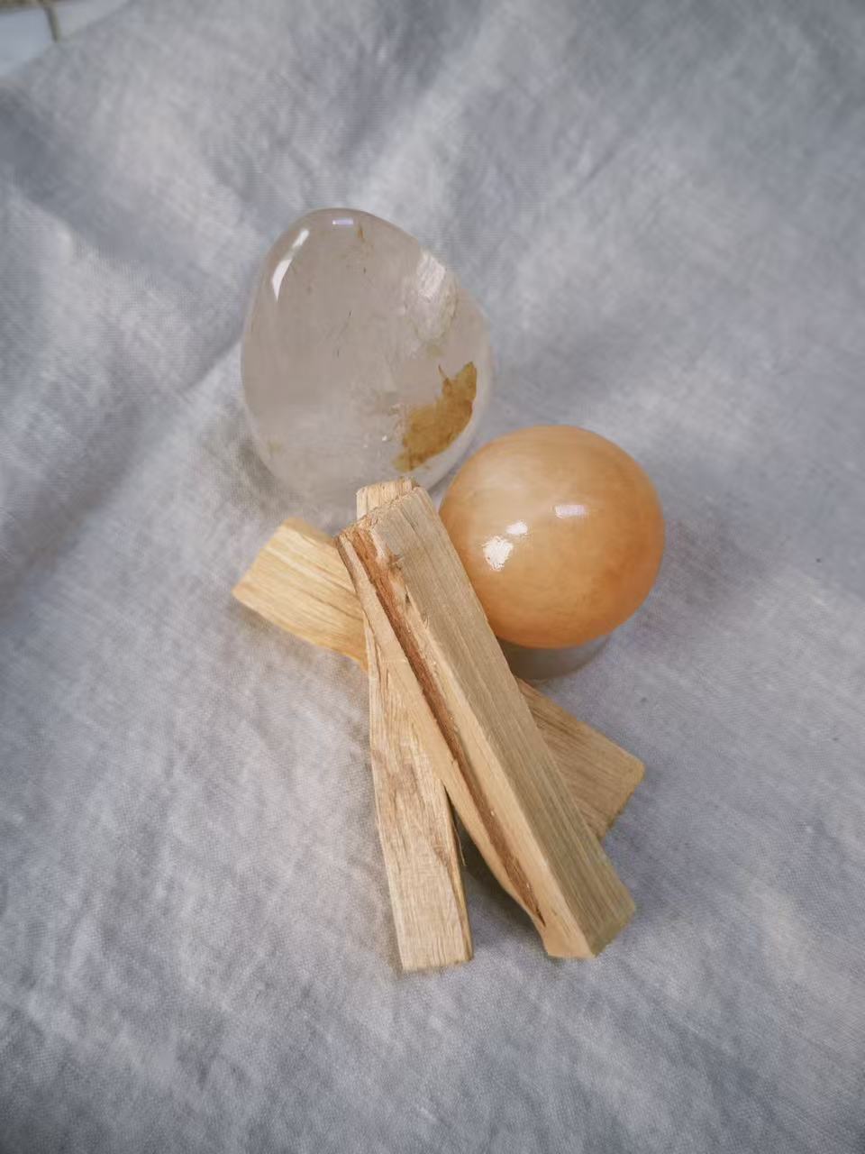 Palo santo sticks with clear quartz and an amber sphere on linen